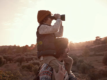 child looking through binoculars on dad's shoulders